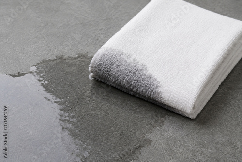 White cotton towel absorbing water from puddle on grey slate, wet and dry contrast