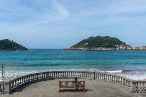 Frau auf einer Bank an der Promenade am Bicentennial Balcony, La Concha Strand, San Sebastián, Spanien