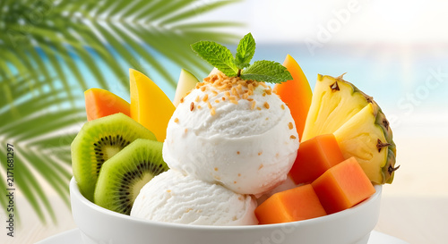 Ice cream scoops are served in a bowl topped with fresh tropical fruits and aromatic mint leaves.