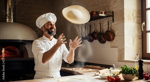 Chef wearing a white uniform tosses fresh pizza dough into the air inside a professional kitchen.