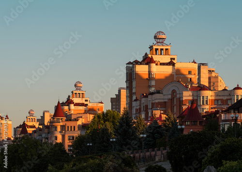 Scenic view of modern residential buildings with red roofs and globes on the roof on Obolon embankment in Kyiv illuminated by warm sunset light.