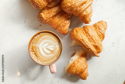 Картината върху платно Fresh buttery croissants and a cup of latte coffee on a white marble table backg