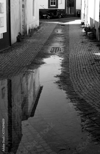 Bild auf Leinwand Building reflection in a puddle on a wet cobblestone alley