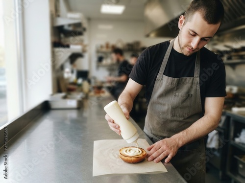 Chef meticulously applies creamy sauce to a fresh burger bun in a professional restaurant kitchen