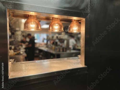 Commercial Kitchen Pass with Warm Pendant Lighting Overlooking a Bustling Culinary Workspace for Restaurant Service and Gourmet Preparation