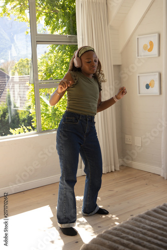 Obraz na plátně Teenage African girl dancing in bedroom near window on wood floor wearing pink h