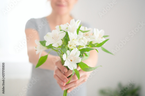 A woman holds a white flower bouquet in her hands in a bright room. The lady cradling blossoms presents a calm, peaceful moment of tender contemplative serenity and pure, delicate beauty indoors.