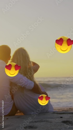 Multiple heart eyes face emoji floating against couple embracing each other at beach
