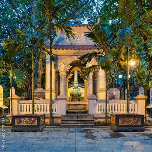King Le Thai To's Temple at dusk in Hanoi, Vietnam, featuring traditional architecture and palm trees illuminated by warm evening lights in the city center