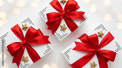 Three white gift boxes with red ribbons and gold stars on festive bokeh lights background