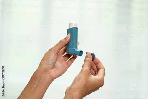 Konstfotografi Close-up of hands holding a blue asthma inhaler and its cap against a soft bright background, showing daily respiratory treatment and healthcare