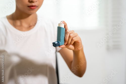 Fotografía Young woman holding a blue asthma inhaler at home, showing respiratory health care, allergy relief and medical treatment