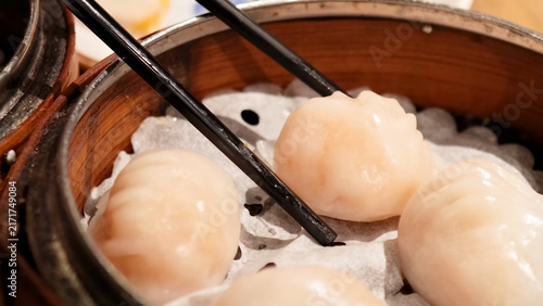 Fotografie Chopsticks Picking Up Steamed Har Gow Shrimp Dumplings in Bamboo Steamer