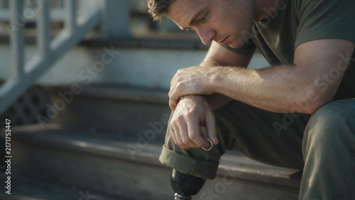 Making difficult decisions, upset young veteran man with prosthetic leg sitting on house porch, divorce poster and legal advice on divorce process, copy space for text