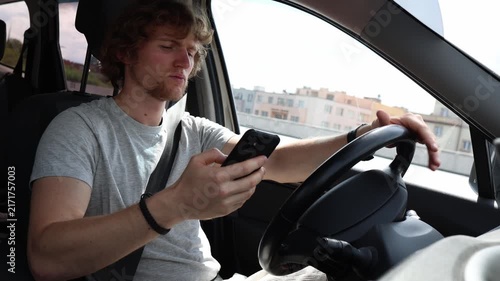 Young driver stares at his smartphone while driving through the city losing focus on the road as phone distraction creates dangerous behavior and high accident risks here