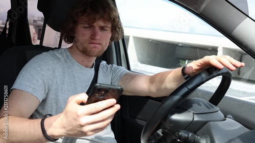 Young driver cannot stop checking his smartphone while driving showing compulsive phone use and dependence that takes attention away from traffic and road safety on trips