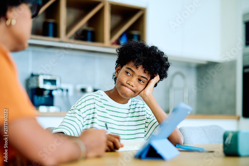 Canvas Print Young Black boy looks bored and unmotivated doing homeschooling schoolwork at ki