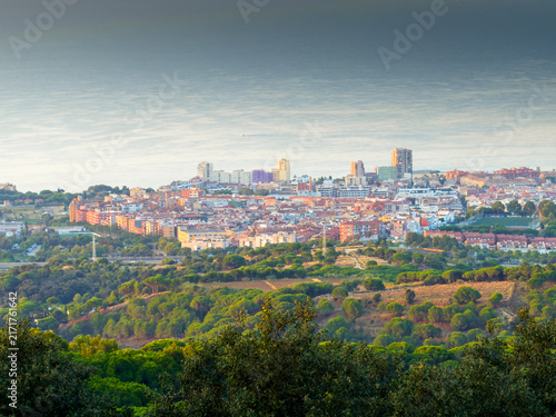 Scenic aerial panoramic view of Mataro coastal city in Catalonia Spain at sunrise, overlooking Mediterranean sea, forested green hills and urban skyline.