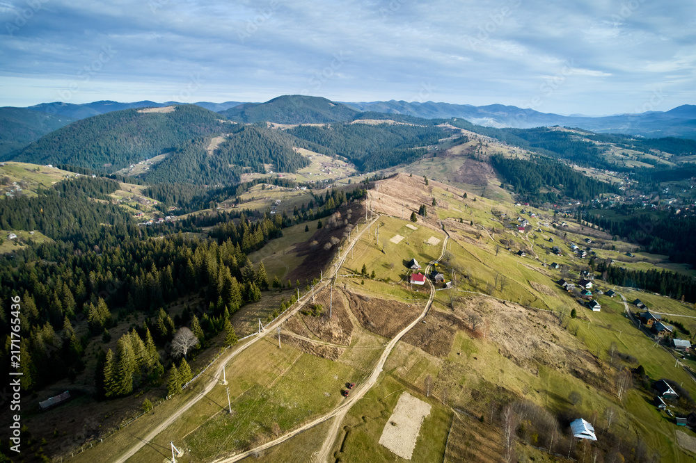Naklejka premium Aerial view of stunning mountain landscape with rolling hills, dense forests, rural houses.
