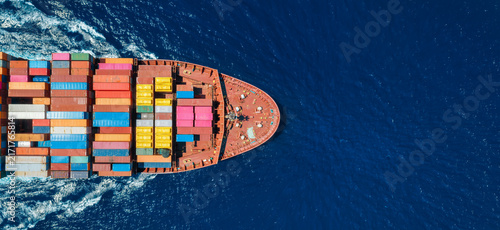 Aerial overhead view of a the bow of a container cargo ship in motion over ocean as a banner for transport and industry with copy space