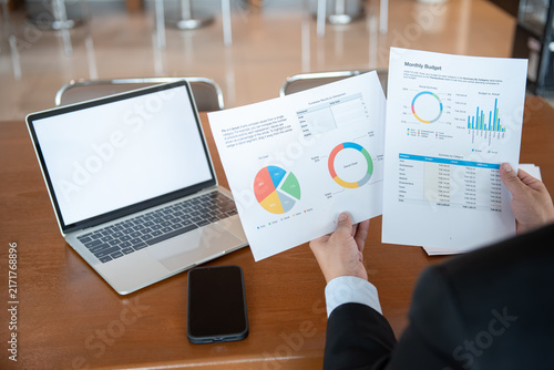 Businessman Reviewing Financial Charts and Monthly Budget Reports with Laptop on Office Desk