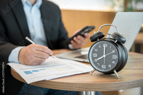 Businessman Working Against Time with Alarm Clock on Desk Reviewing Financial Documents