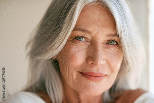A smiling elderly woman, with gray hair and wrinkles, has a healthy glow and expressive face, captured in a close-up portrait under natural light