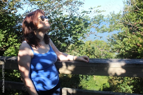 Relaxed Mature Woman Enjoying Sunlight in Nature Park with Dappled Shadows

