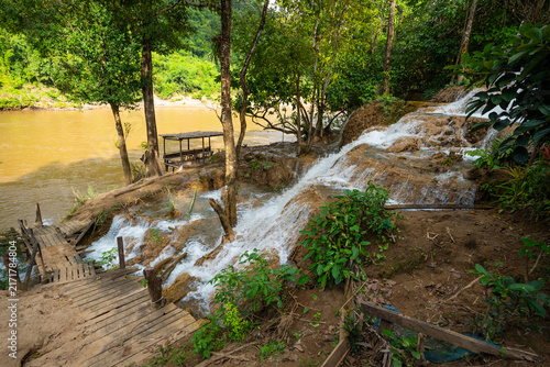 Fotografie Scenic limestone cascading waterfall at Naw Ta or No Taw in Karen State, Myanmar, surrounded by lush green tropical forest, wooden path, and river stream in bright daylight