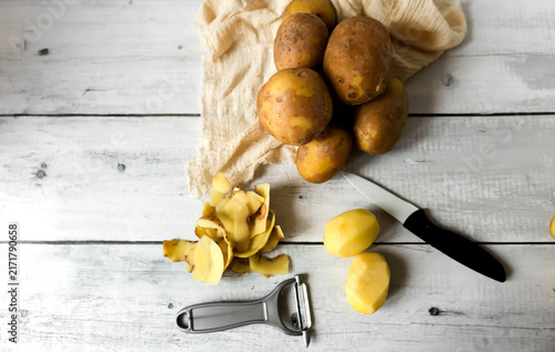 Foto Peeling raw potatoes with a knife and vegetable peeler on a white wooden table