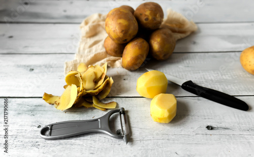 Bild auf Leinwand Peeling raw potatoes with a knife and vegetable peeler on a white wooden table