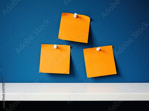 Three orange sticky notes pinned to a dark blue wall suitable for planning media symbolizing task organization brainstorming and new ideas