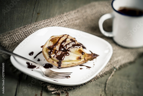 Pear puff pastry on plate with mug of chocolate sauce, close up