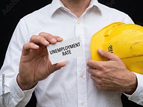 Worker holding an unemployment rate card and hard hat ideal for financial news representing job loss economic crisis and labour market decline