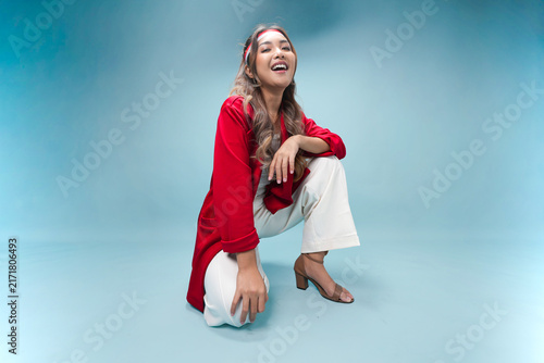 Pretty Indonesian woman is sitting on the floor and posing smiling to the camera.