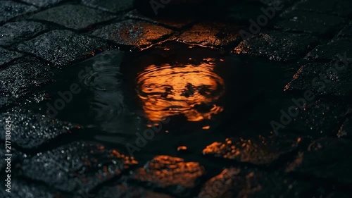 Atmospheric 4K Cinematic Seamless Loop Glowing Halloween Pumpkin Face Reflection Rippling in a Rain Puddle on Dark Wet Cobblestone Street at Night