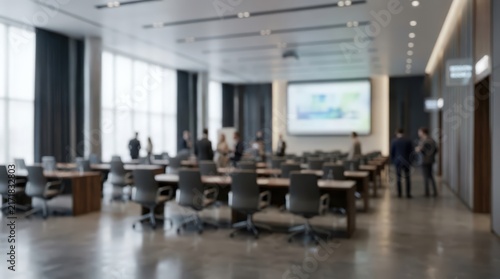 Blurred business professionals gather in a spacious conference room for a corporate meeting. Rows of chairs and tables face a projection screen in a bright, modern office environment.