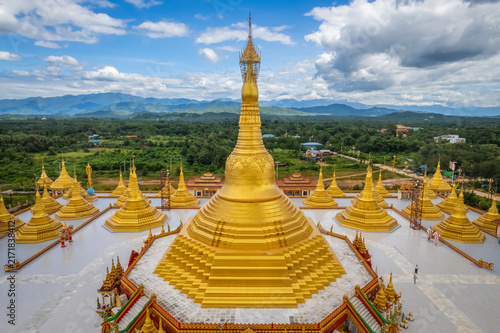 Фотография Aerial view of a golden stupa surrounded by smaller pagodas with lush green hill
