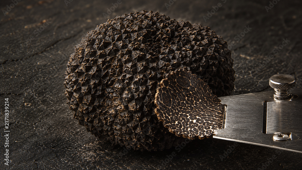 Fototapeta premium Black Périgord truffle extreme macro showing diamond-faceted warty exterior surface with interior marble slice revealing cream vein network on dark charcoal luxury food editorial