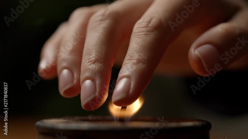 A close-up shot shows a person's fingers gently interacting with a candle flame before extinguishing it, with smoke rising.