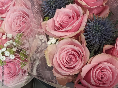 Fresh festive floral arrangement featuring soft pink roses and blue sea holly flowers