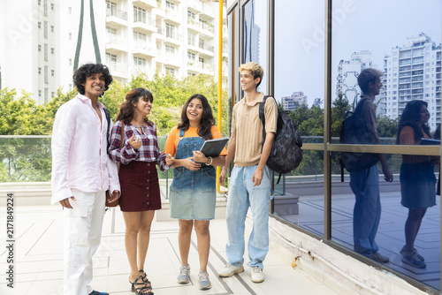 Diverse group of indian gen z college students enjoy conversing outdoors on campus, holding notebooks and wearing backpacks, representing education, friendship, and learning together