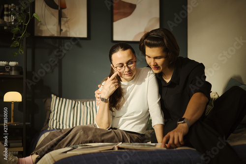 Obraz na płótnie Young diverse couple sitting on bed and looking at photo album together, remembering memories