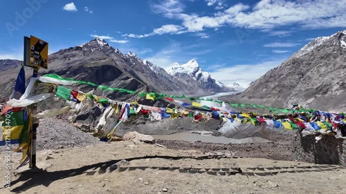 Zanskar, India : Panoramic footage of tibetan buddhist prayer flags blown by wind with Drang Drung glacier, long river ice in Zanskar valley of Ladakh, Indian Himalayas