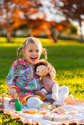 happy girl playing with wooden tea set toys and doll outdoors having a pretend picnic