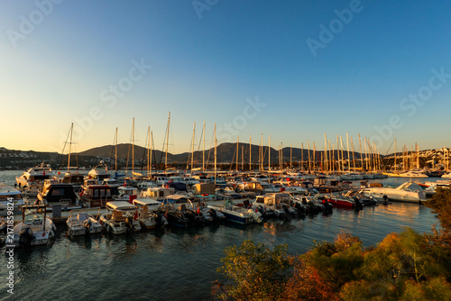 Картината върху платно Marina filled with numerous docked yachts and boats, reflecting warm golden light from the setting sun