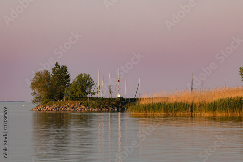 Fonyod, Hungary: Harbor pier with a communication tower and a sailboat on Lake Balaton at sunset, with distant hills and Szigliget Castle silhouette.