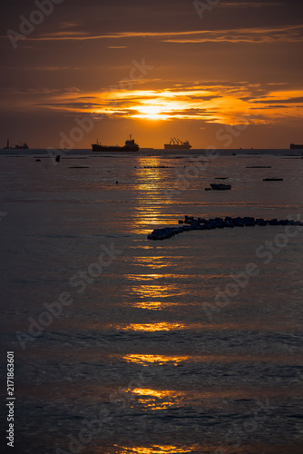 Sunset Over the Shipping Lanes: Majestic cargo ships silhouette against a dramatic sunset on the horizon, their reflections shimmering on the calm ocean surface.