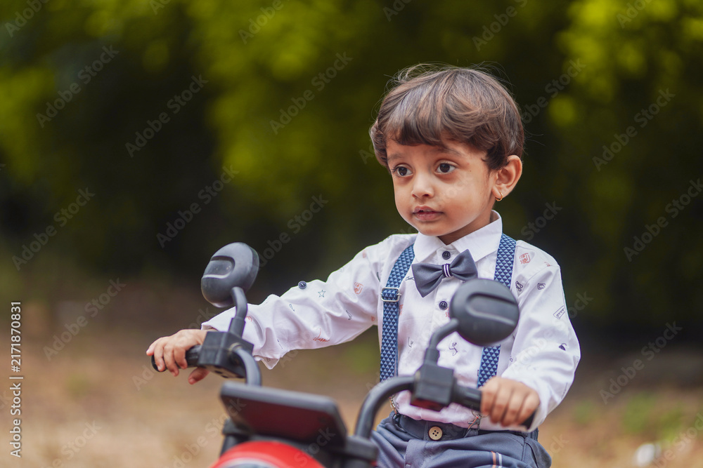 Fototapeta premium A cute Indian little boy in a stylish outfit enjoys riding a red