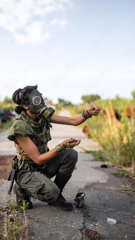 Fototapeta premium A resilient survivor wearing a gas mask crouches on a ruined road, searching for hope in a bleak, postapocalyptic wasteland. Evokes feelings of suspense, survival, and isolation.
